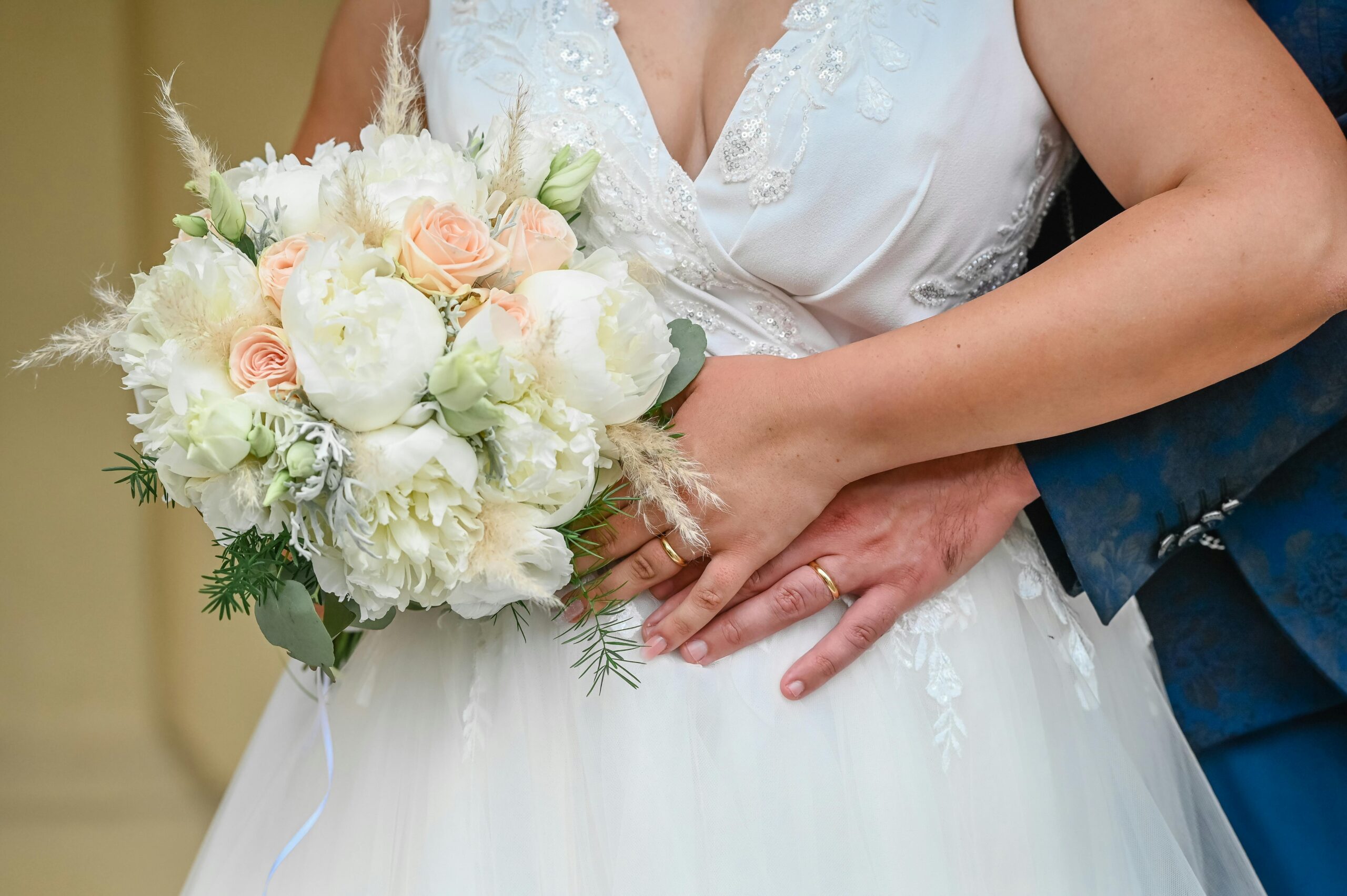 Close-up of bride and groom with elegant bouquet, showcasing wedding rings in an intimate pose.